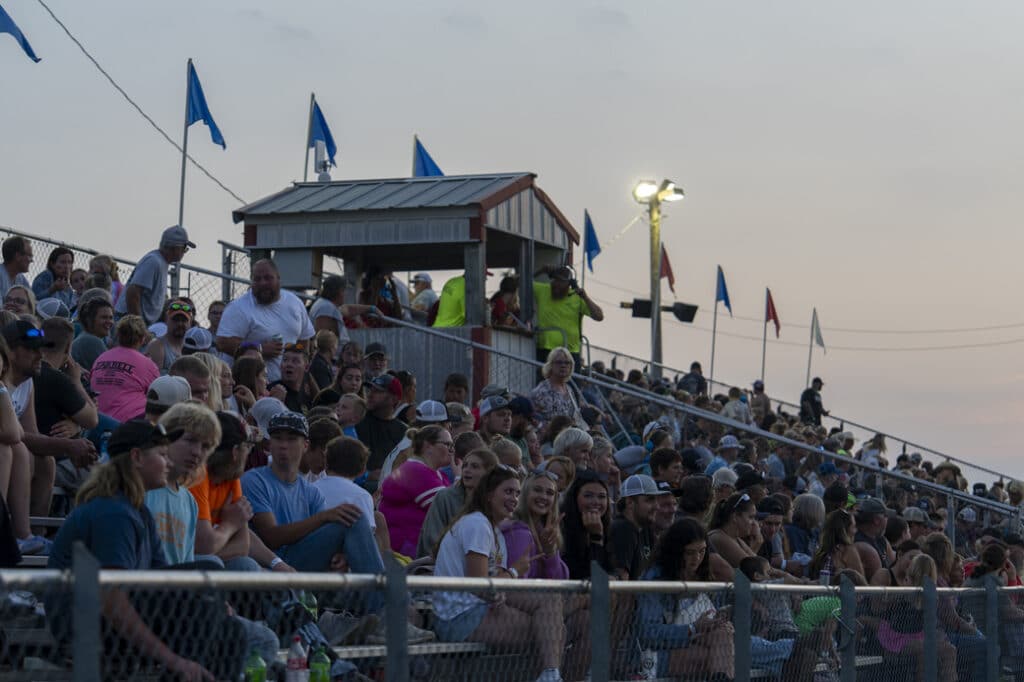 A large crowd fills the grandstand at the fairgrounds, watching an event as the evening sky begins to set.