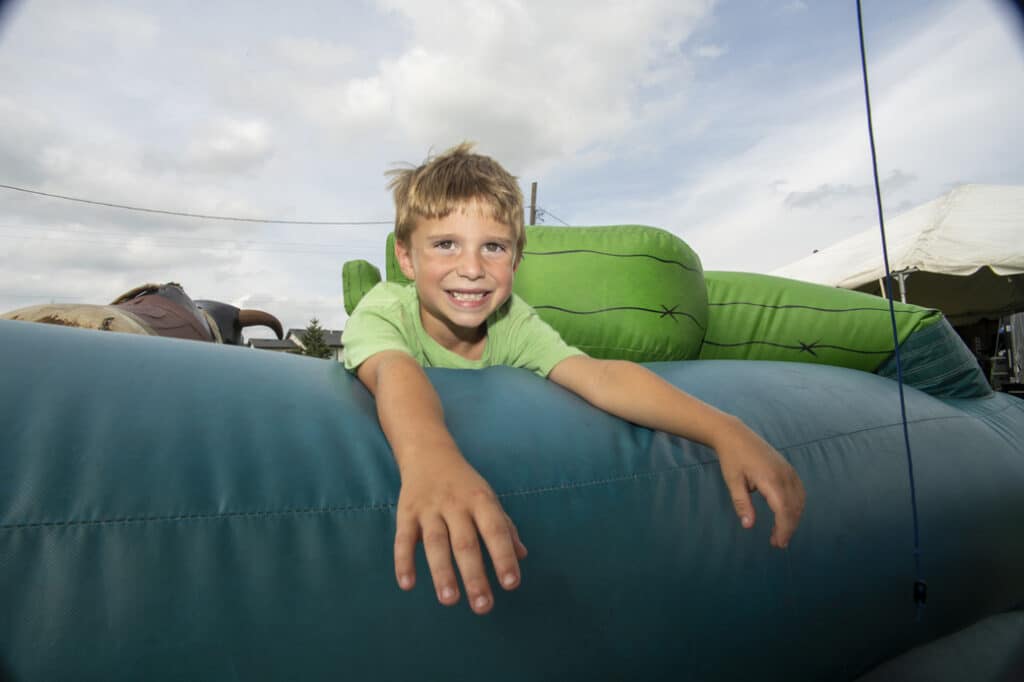 A smiling young boy leans over an inflatable ride at a fair, enjoying a fun and playful moment.